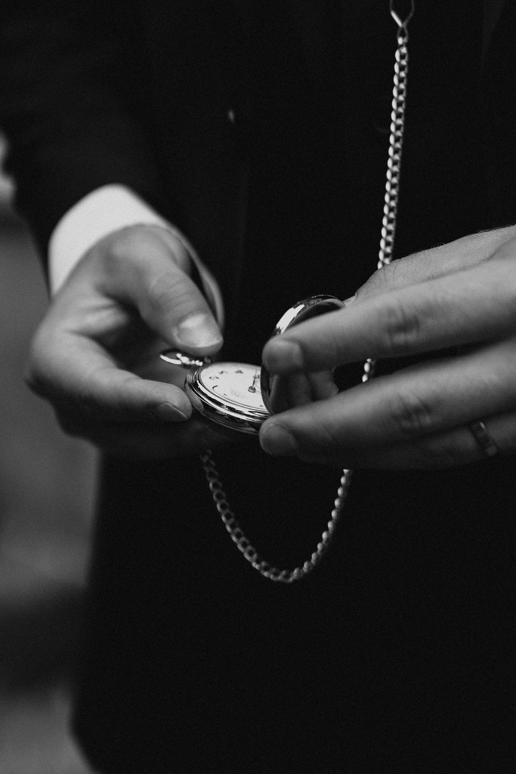Black and white close-up of groom holding an open pocket watch with chain at wedding.