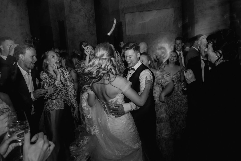 Bride and groom share a romantic first dance surrounded by wedding guests in elegant black and white photography.