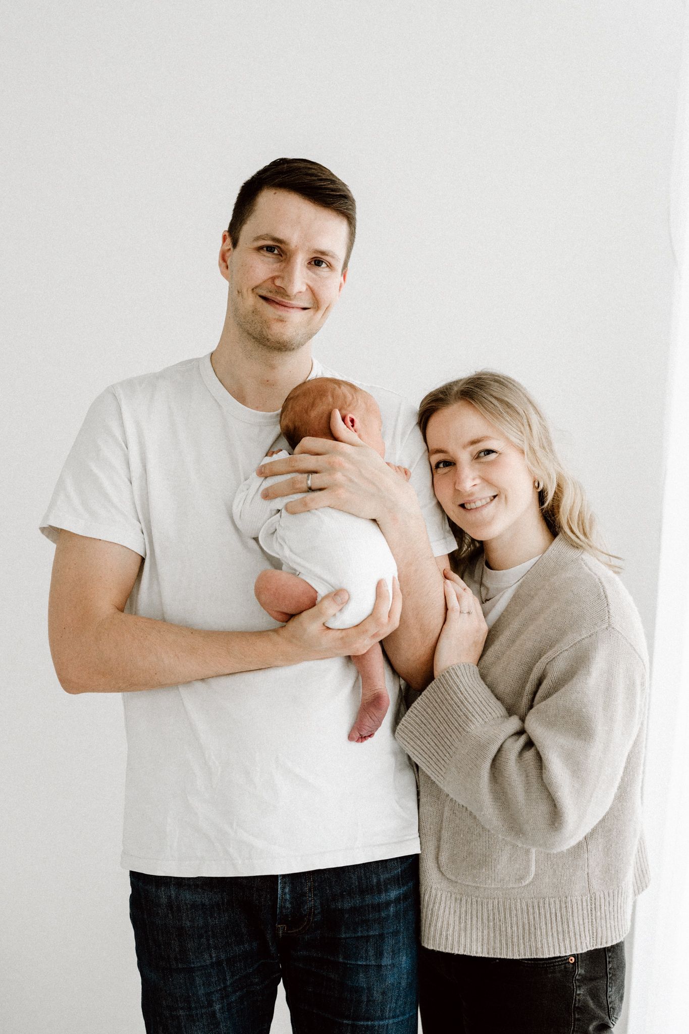 Smiling young couple in casual clothes posing together while father holds their newborn baby.