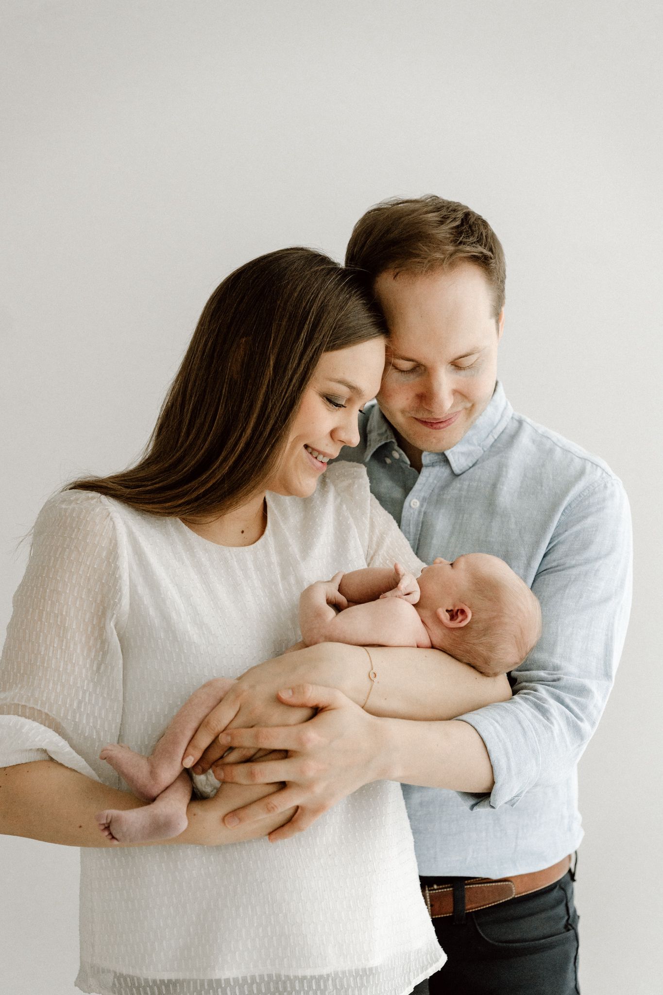 Happy couple in casual attire smiling together while cradling their newborn baby.