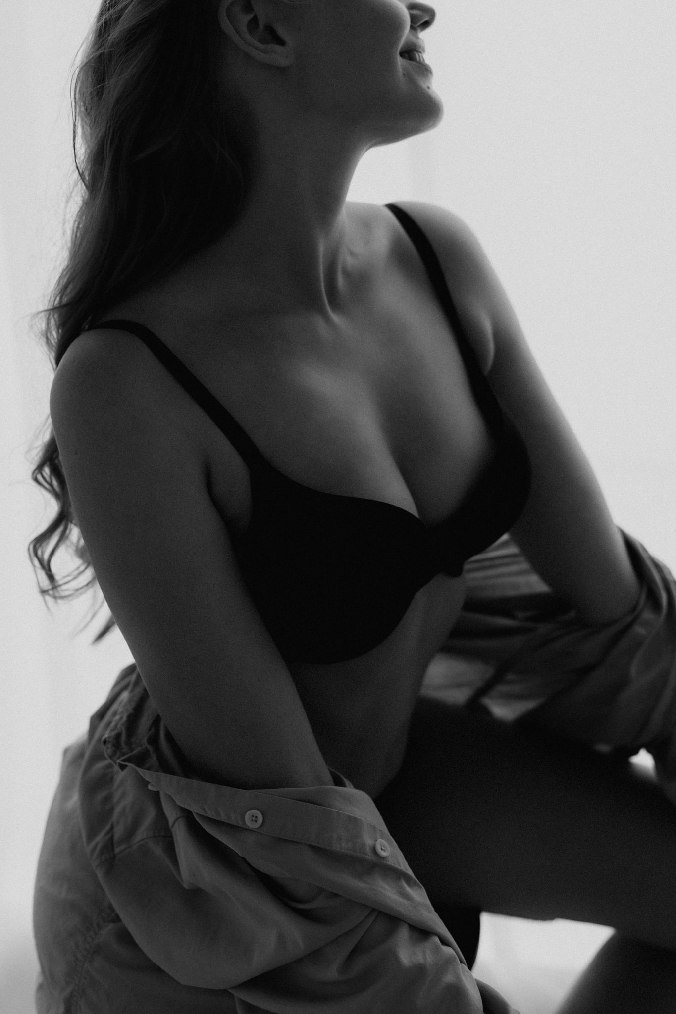 Artistic black and white silhouette of woman in black bra and open shirt posing dramatically.