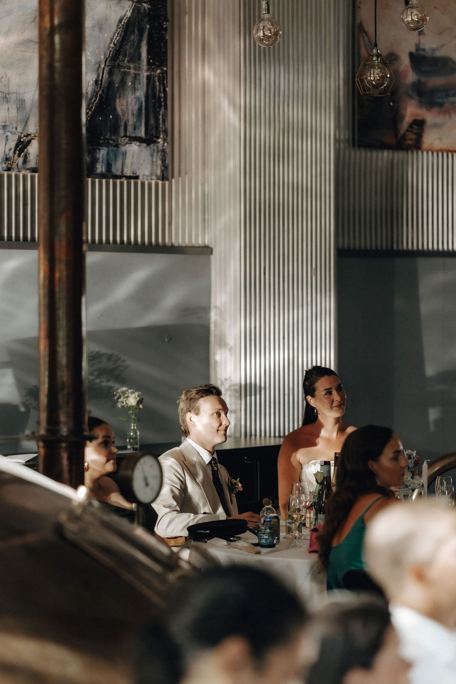 Bride and groom seated at wedding reception table in industrial brewery venue with artwork.