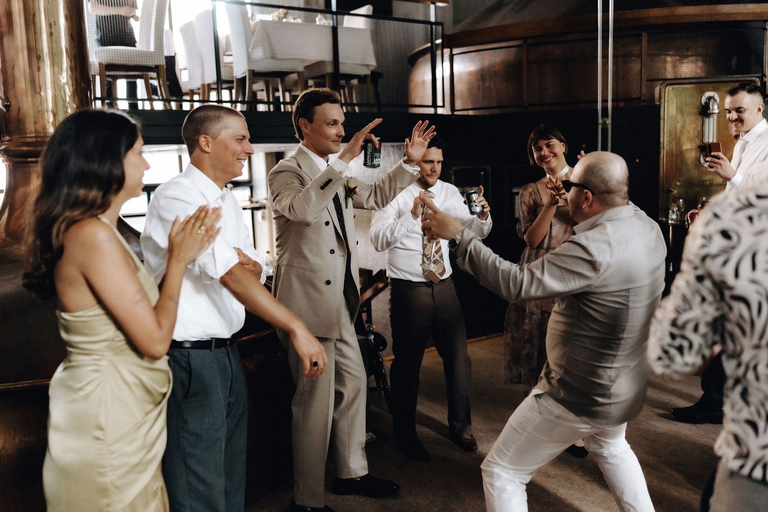 Groomsmen celebrate and dance energetically at a wedding reception in industrial venue.