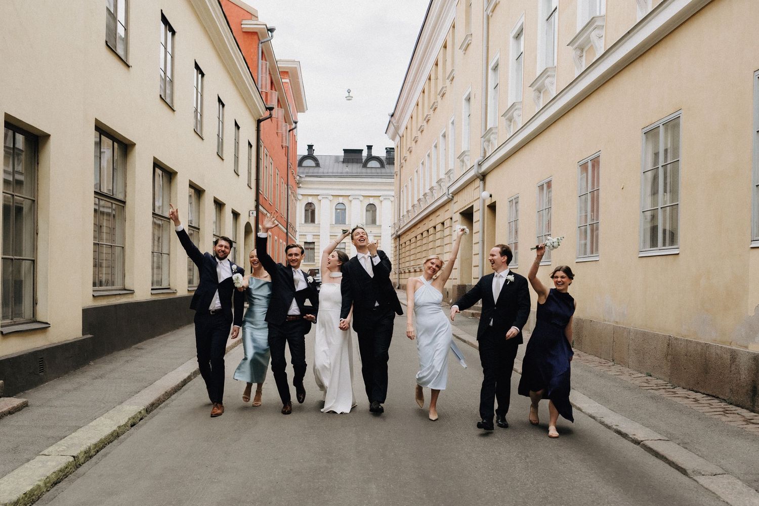 Jubilant wedding party celebrates walking down charming European cobblestone street together.