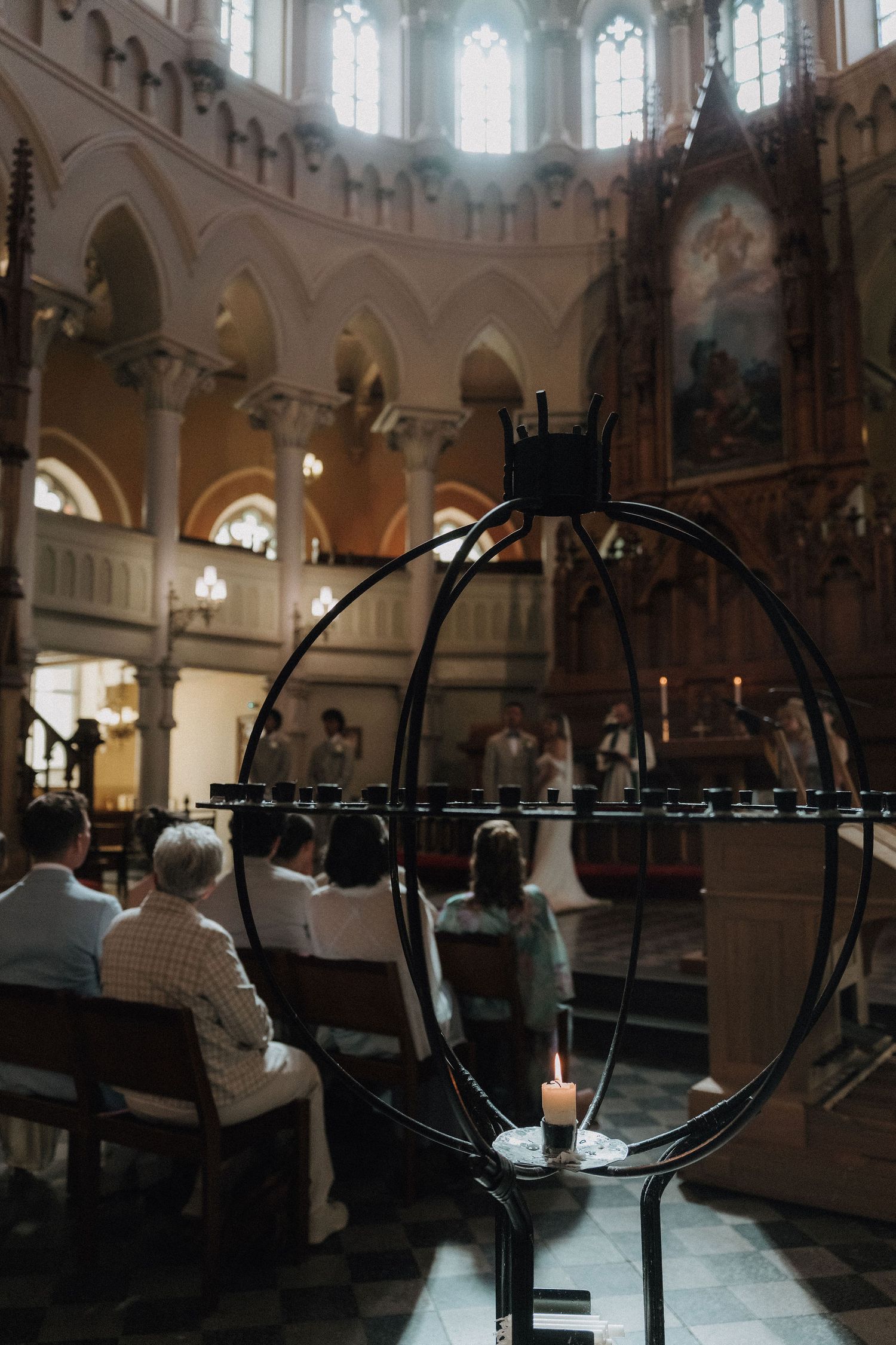 Church wedding ceremony viewed through iron candelabra with lit candle in foreground.