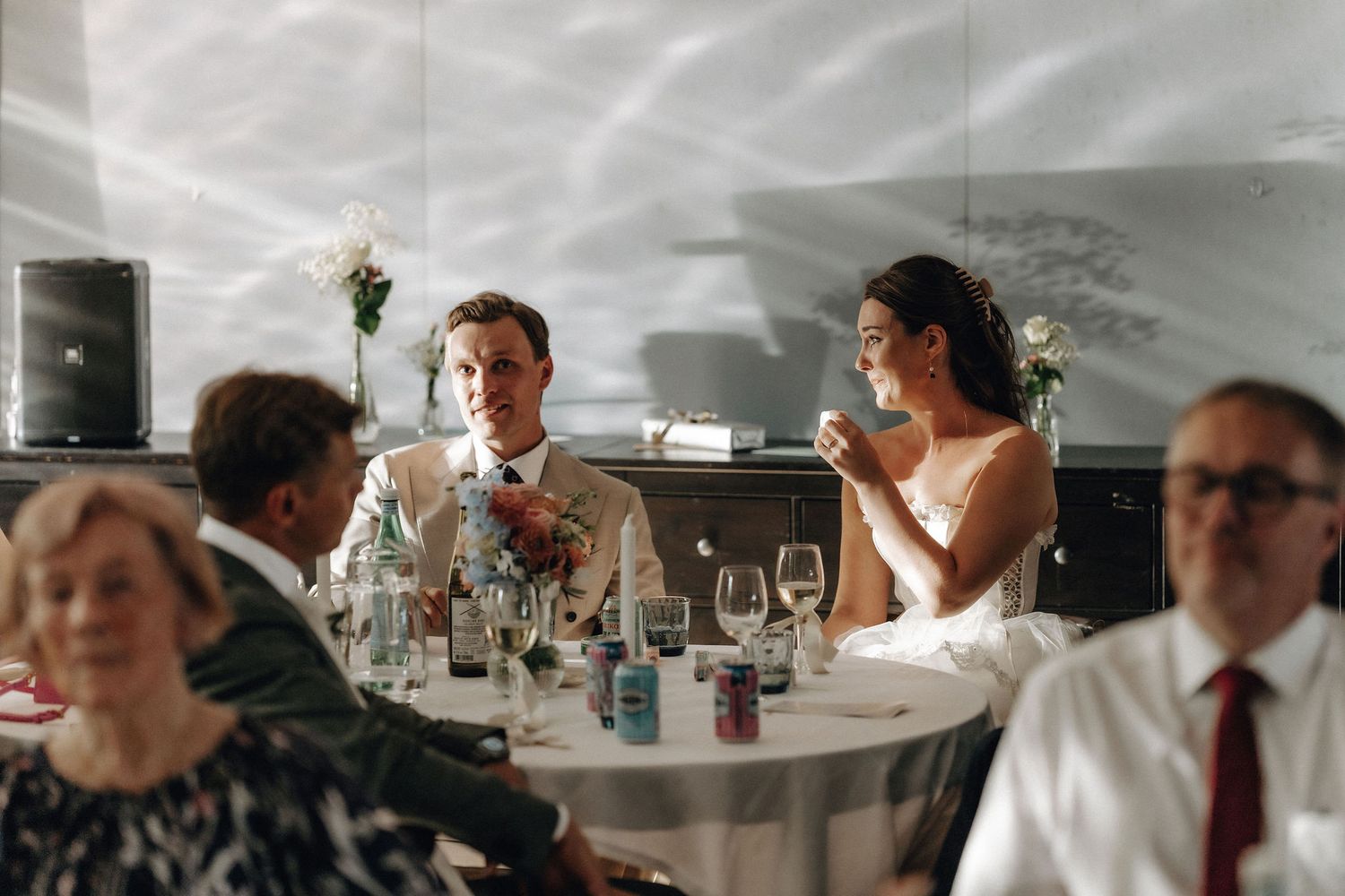 Bride and groom seated at wedding reception table with guests during dinner celebration.