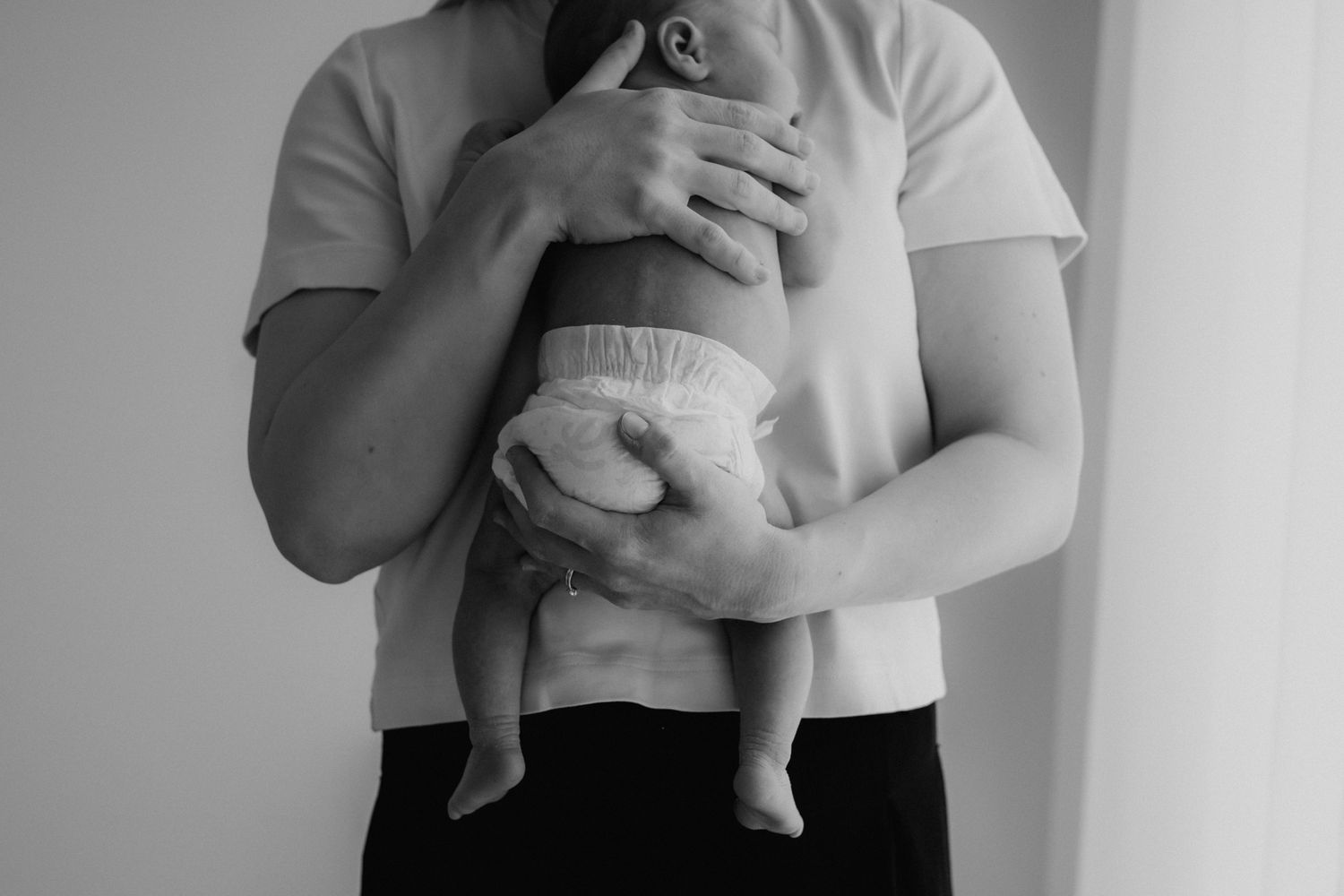 Black and white photo of mother holding newborn baby against her chest tenderly.