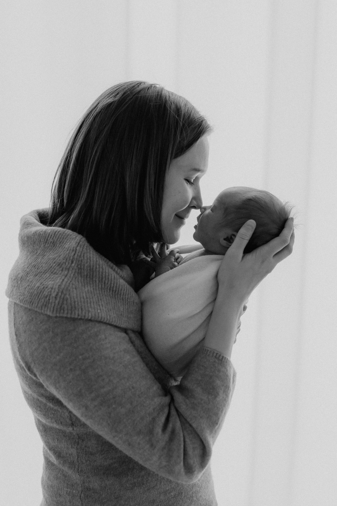 Black and white image of a smiling mother holding her newborn baby face to face tenderly.