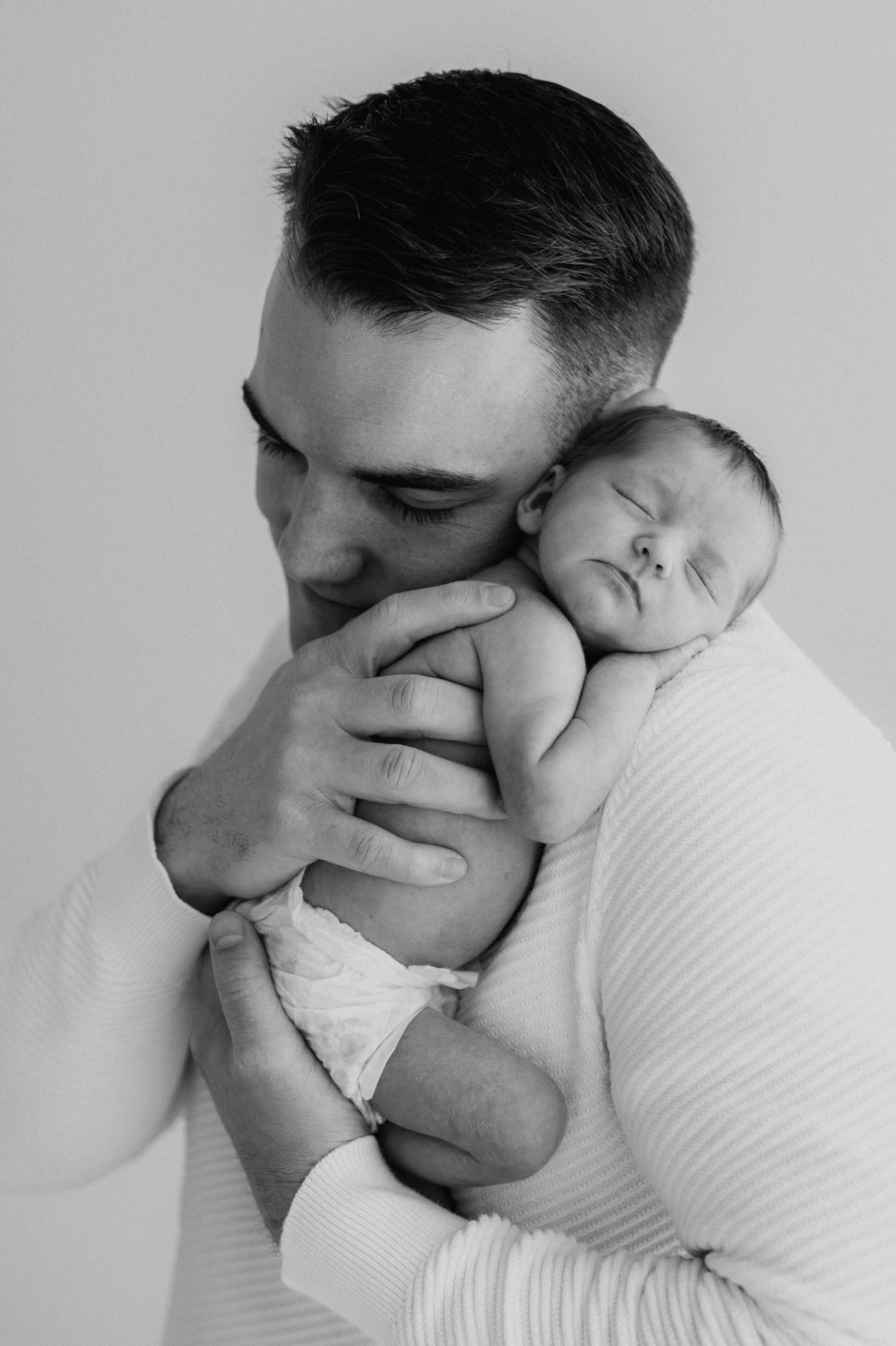 Black and white photo of father kissing newborn baby resting on his chest.