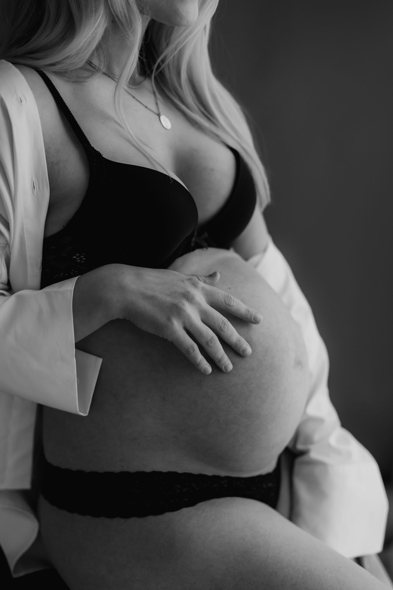 Black and white close-up of pregnant woman in black lingerie and white shirt cradling bare baby bump.