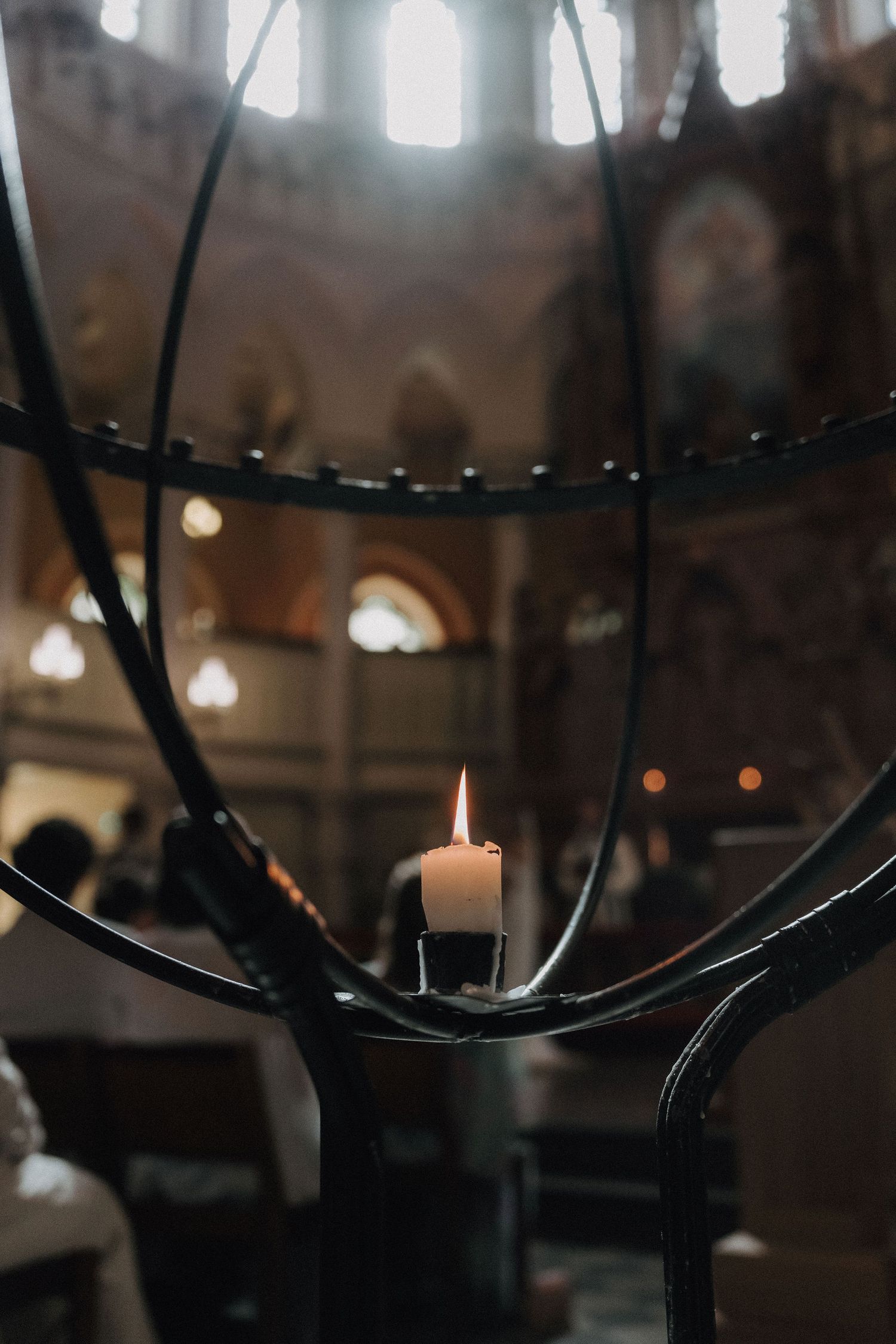 Single white candle burning in decorative iron candelabra inside ornate church.