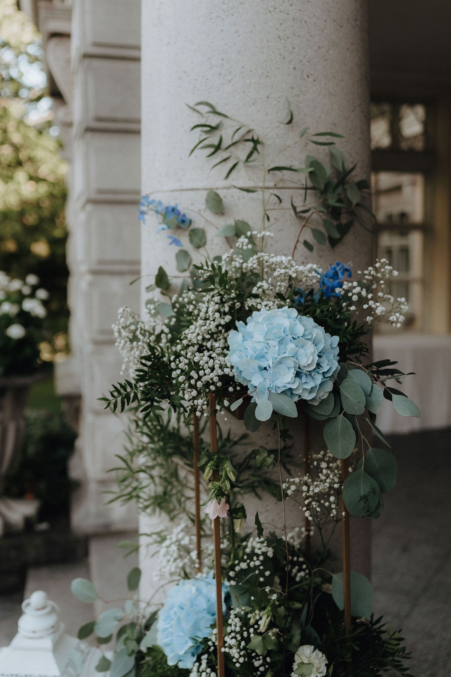 Close-up of blue hydrangea and white baby breath floral arrangement against a stone column.