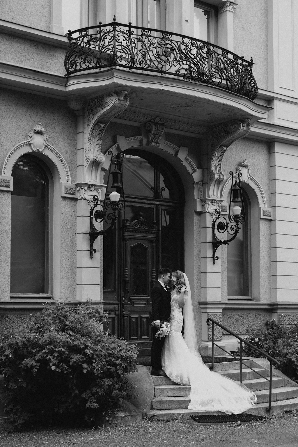 Black and white photo of bride and groom sharing intimate moment at entrance of ornate Art Nouveau building.