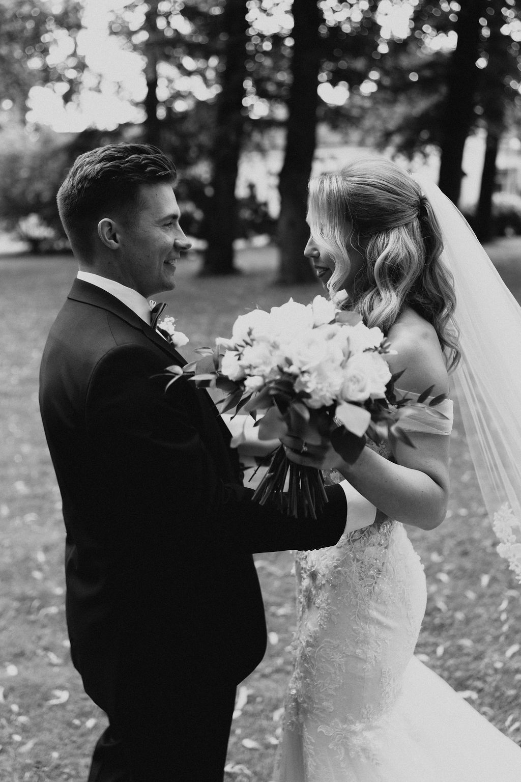 Joyful bride and groom sharing a laugh while holding white floral bouquet, black and white photo.