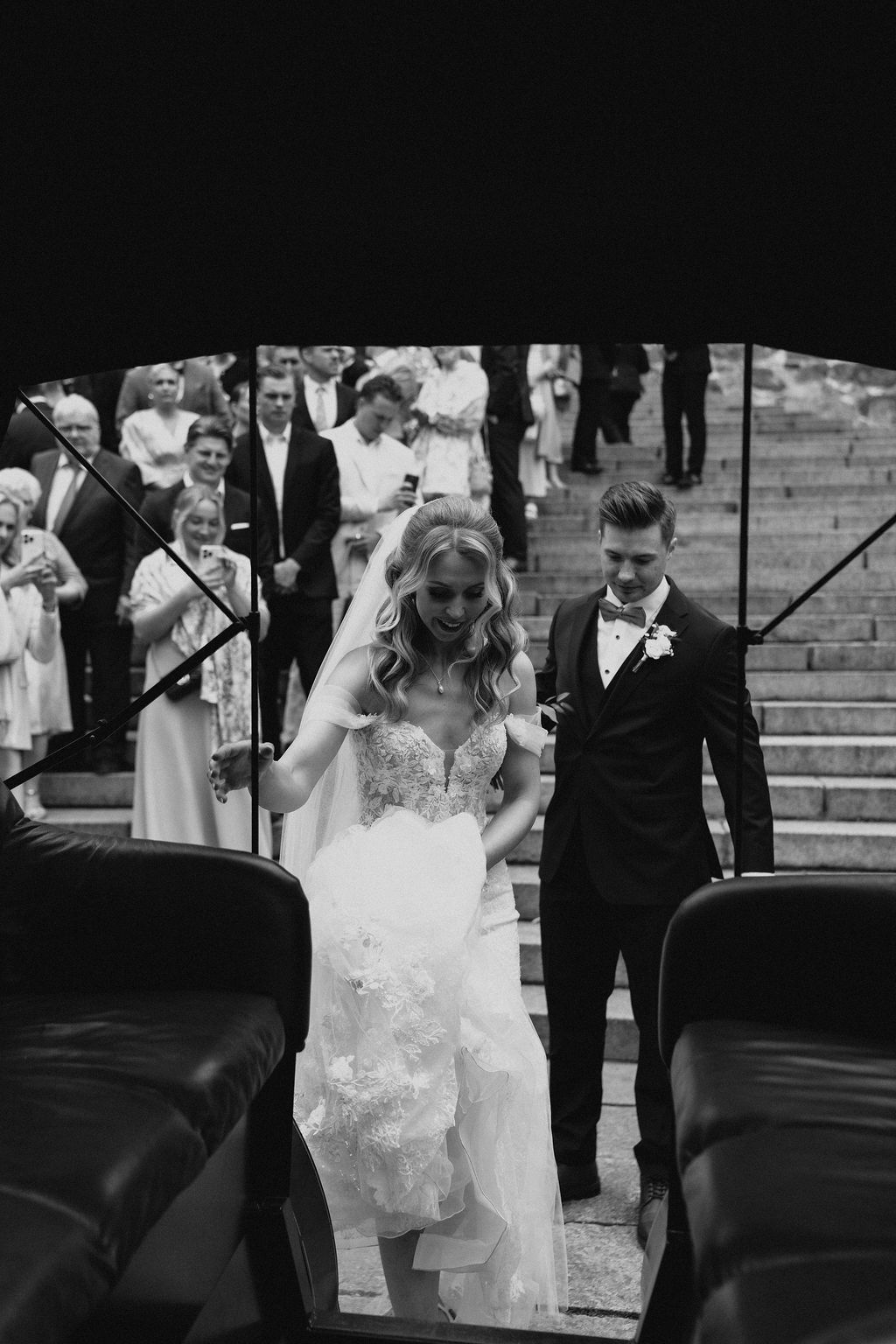 Black and white photo of bride and groom boarding vintage horse-drawn carriage after church ceremony.