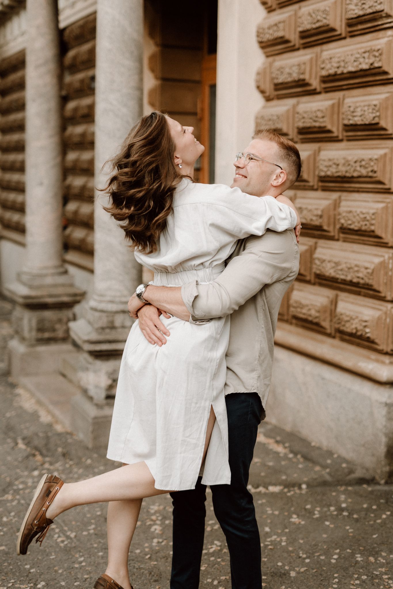 Joyful couple embracing and spinning outside a rustic stone building with decorative facade.