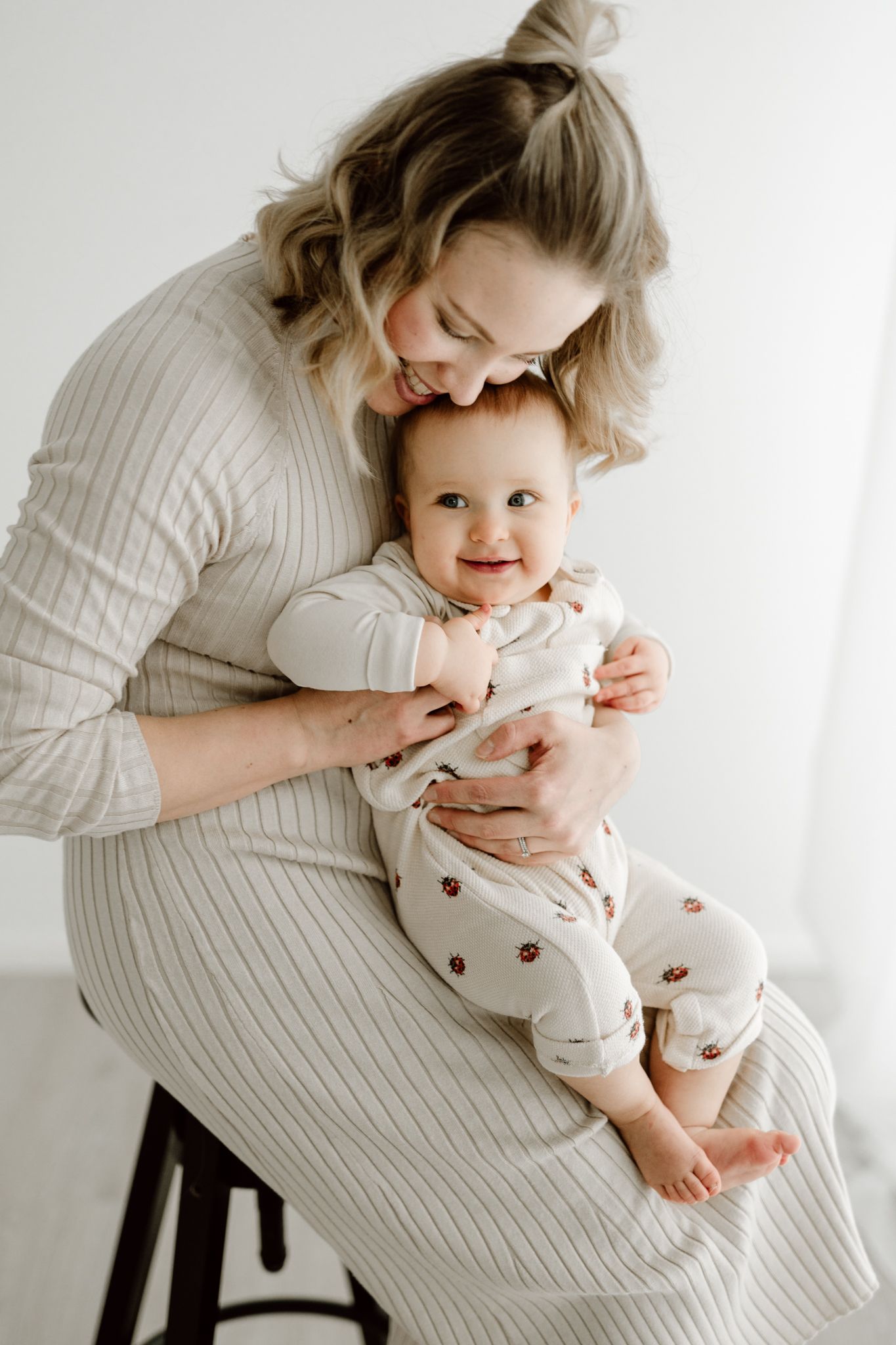 Young mother sitting and cuddling her smiling baby dressed in a floral onesie.
