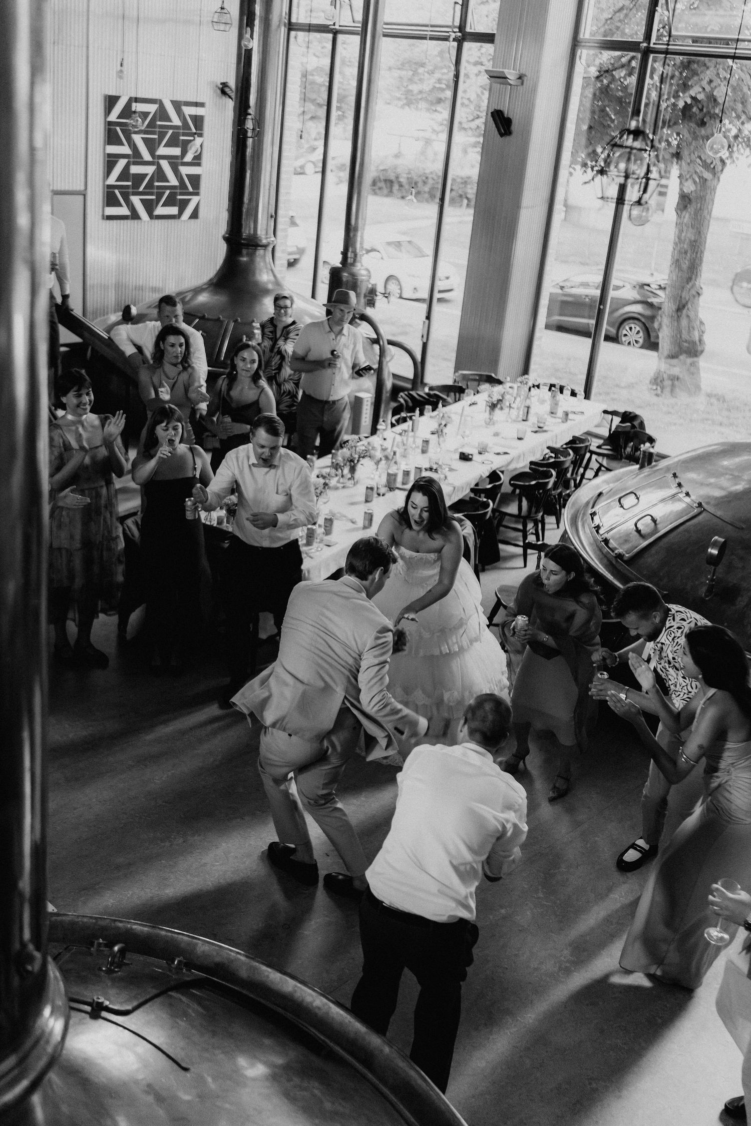 Black and white overhead shot of bride and groom dancing with guests at brewery wedding.