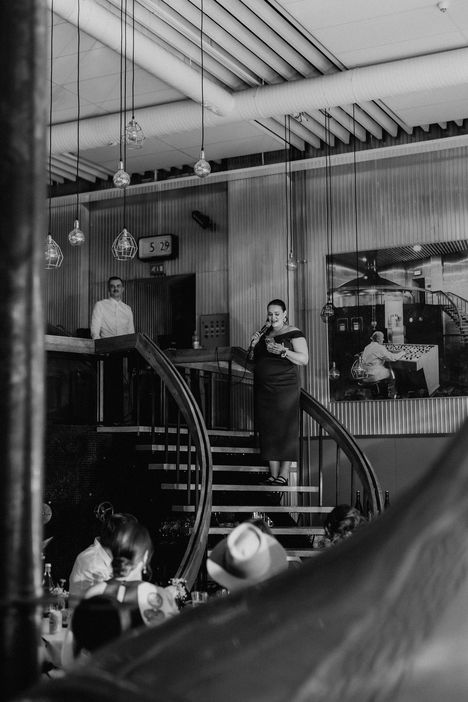 Black and white photo of woman giving speech on staircase at elegant wedding reception venue.