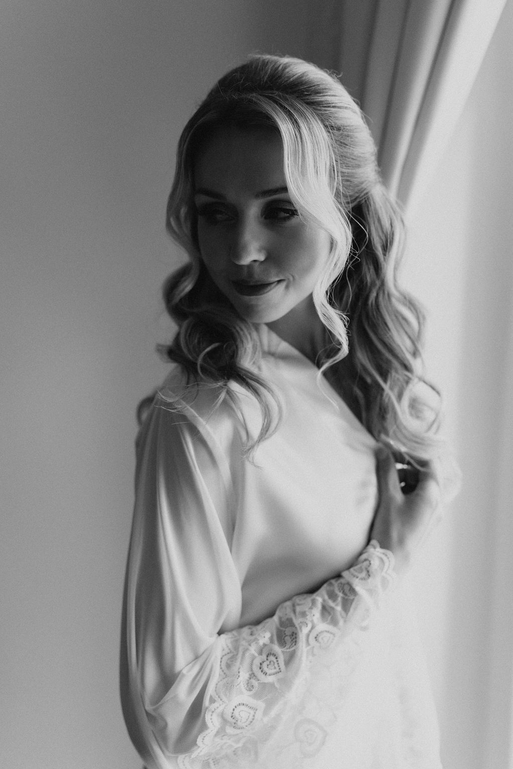 Elegant black and white portrait of smiling bride in white lace robe with flowing curled hair.