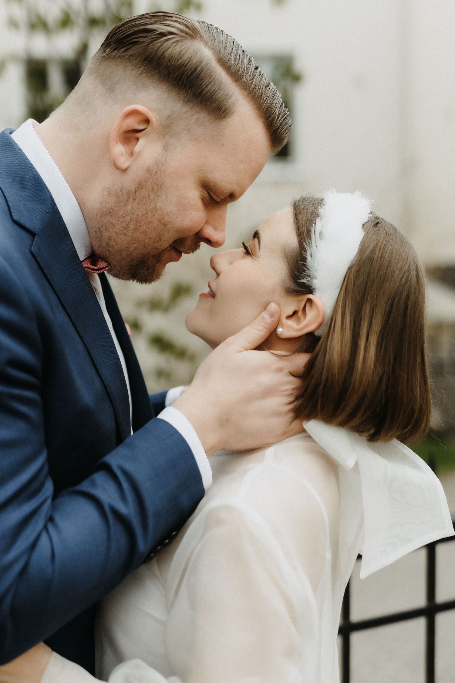 Groom in blue suit tenderly cupping brides chin as they lean in for a kiss outdoors.