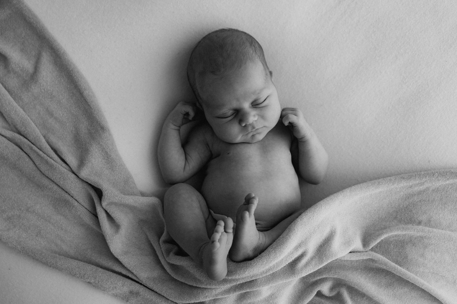 Black and white overhead photo of sleeping newborn baby wrapped in soft blanket.