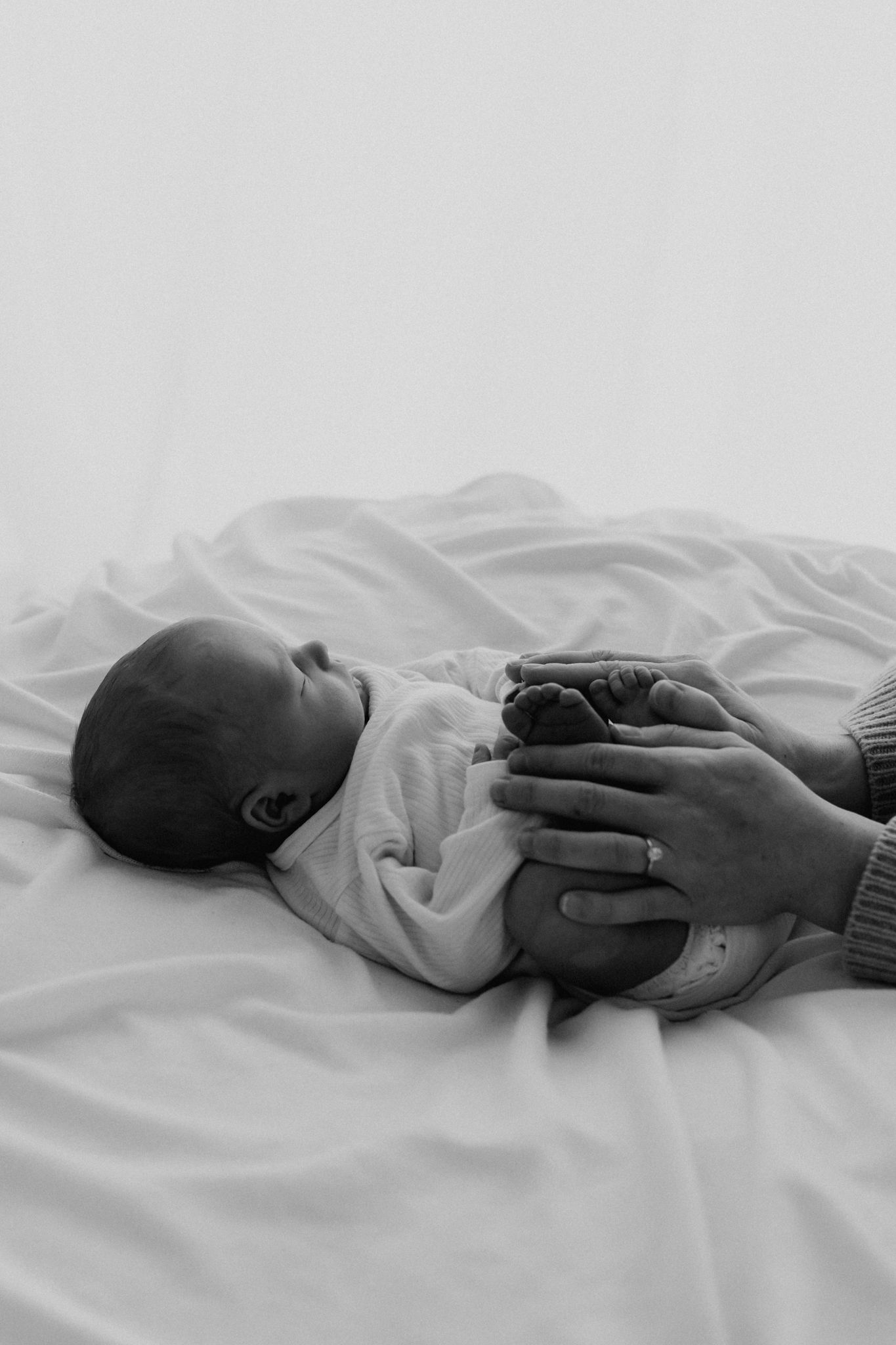 Black and white image of a sleeping newborn lying on white fabric with a parent's hands cradling it.