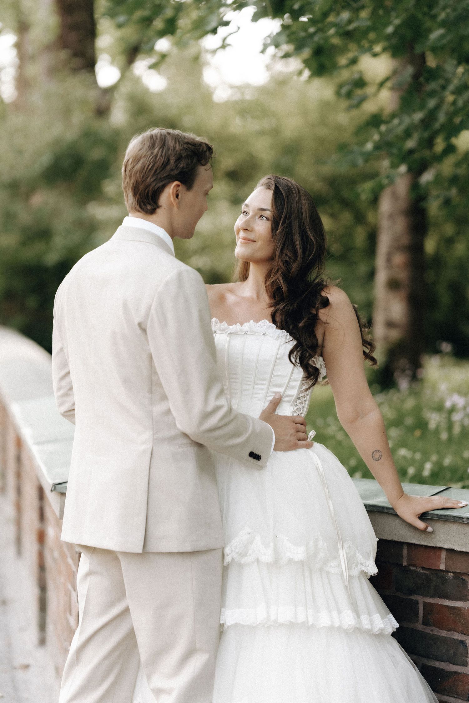 Bride in tiered white gown and groom in ivory suit sharing romantic moment in garden.