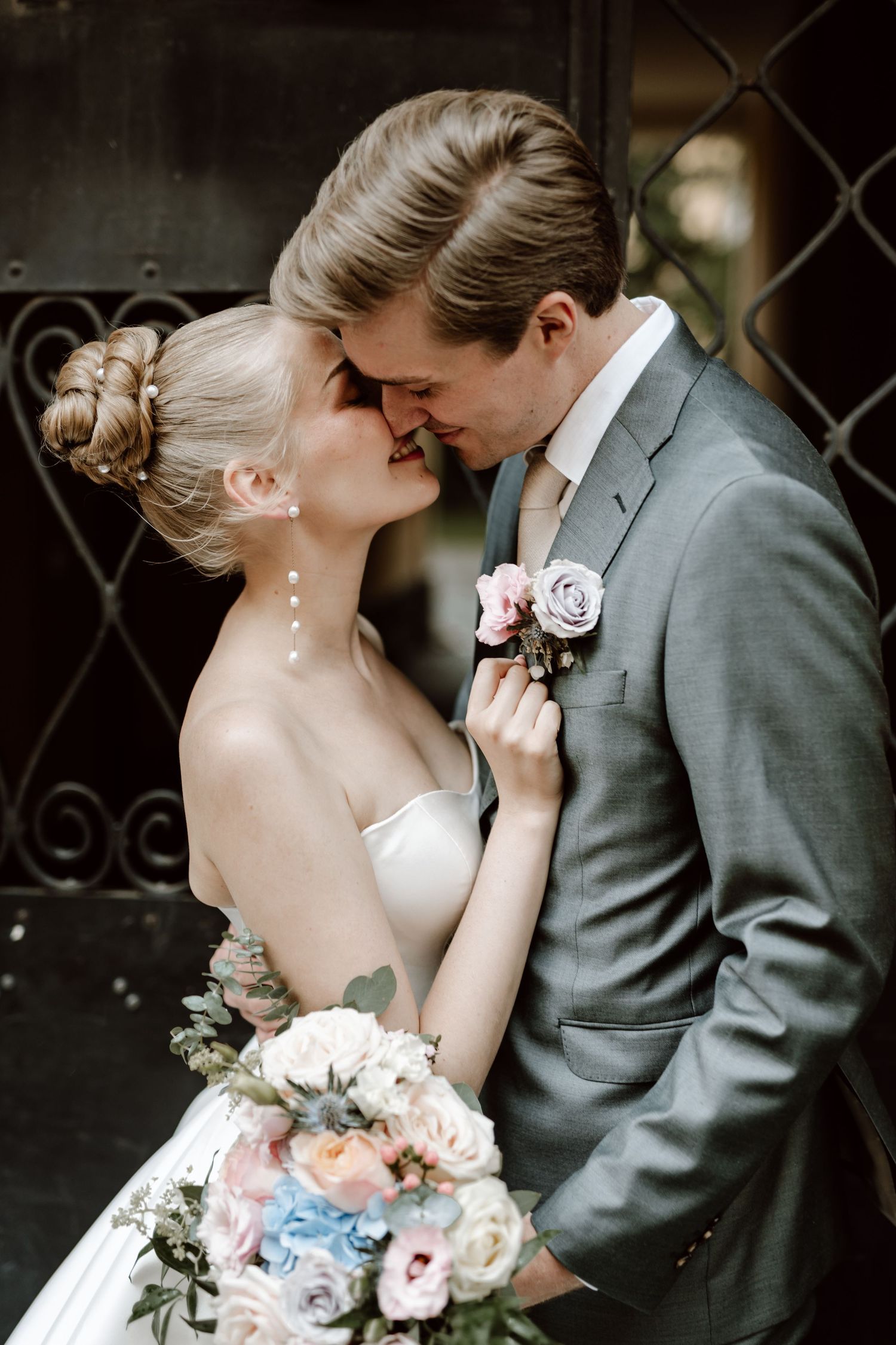 Wedding couple sharing an intimate almost-kiss, bride holding colorful bouquet of pink and blue flowers.