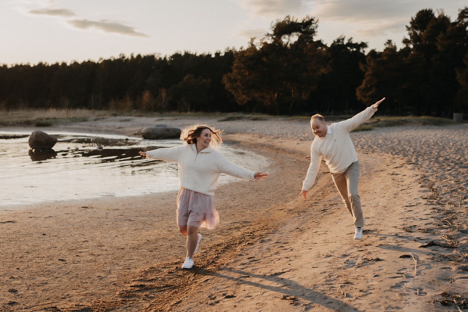 Two children playing joyfully on a sandy beach at golden hour with forest in background.