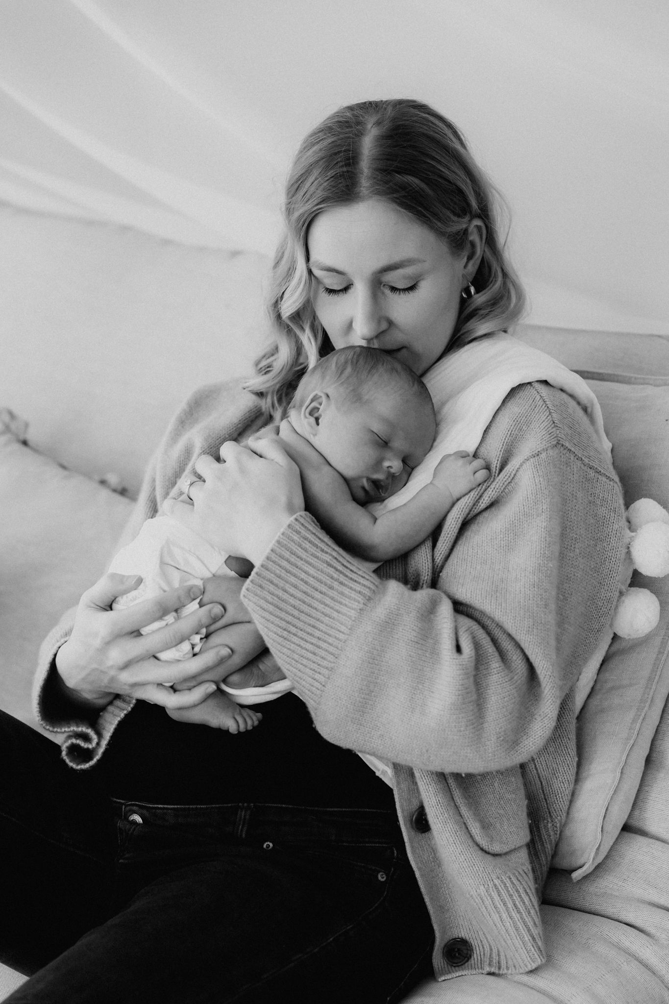Black and white photo of a mother in cozy sweater tenderly holding her sleeping newborn baby.