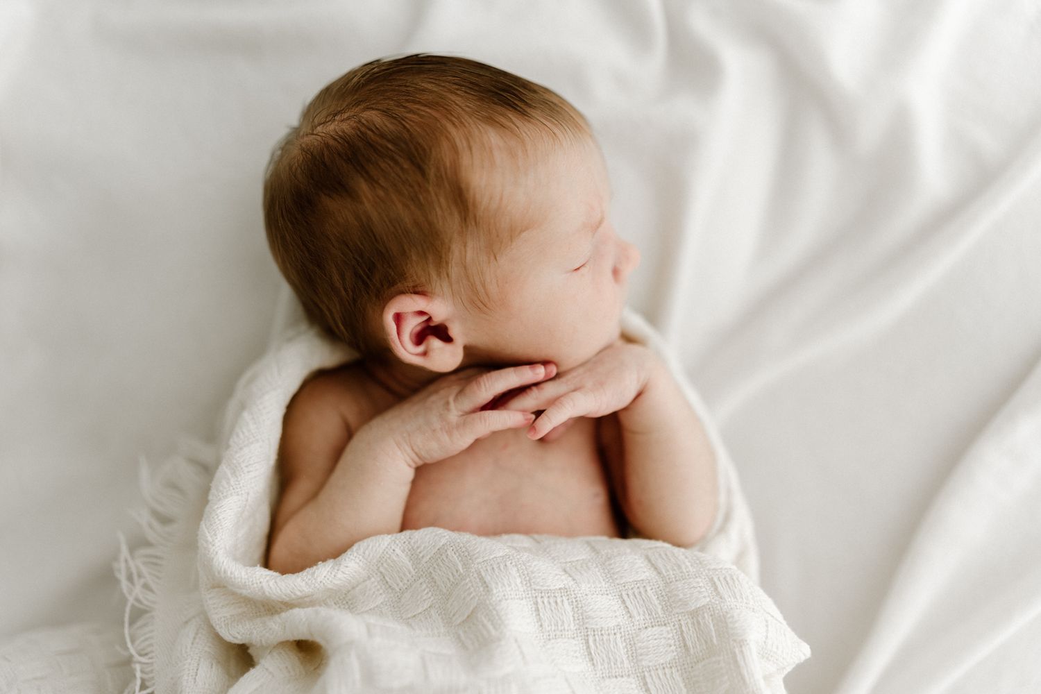 Peaceful sleeping newborn baby rests on soft white textured blanket in a serene close-up portrait photo.