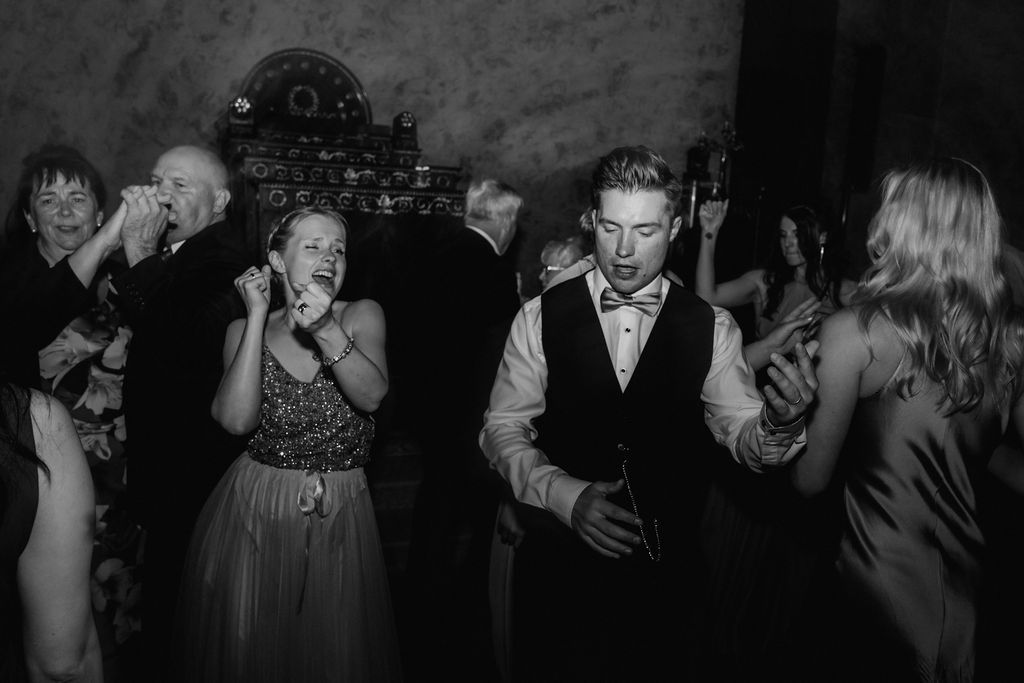 Guests laugh and dance energetically at wedding reception in black and white.