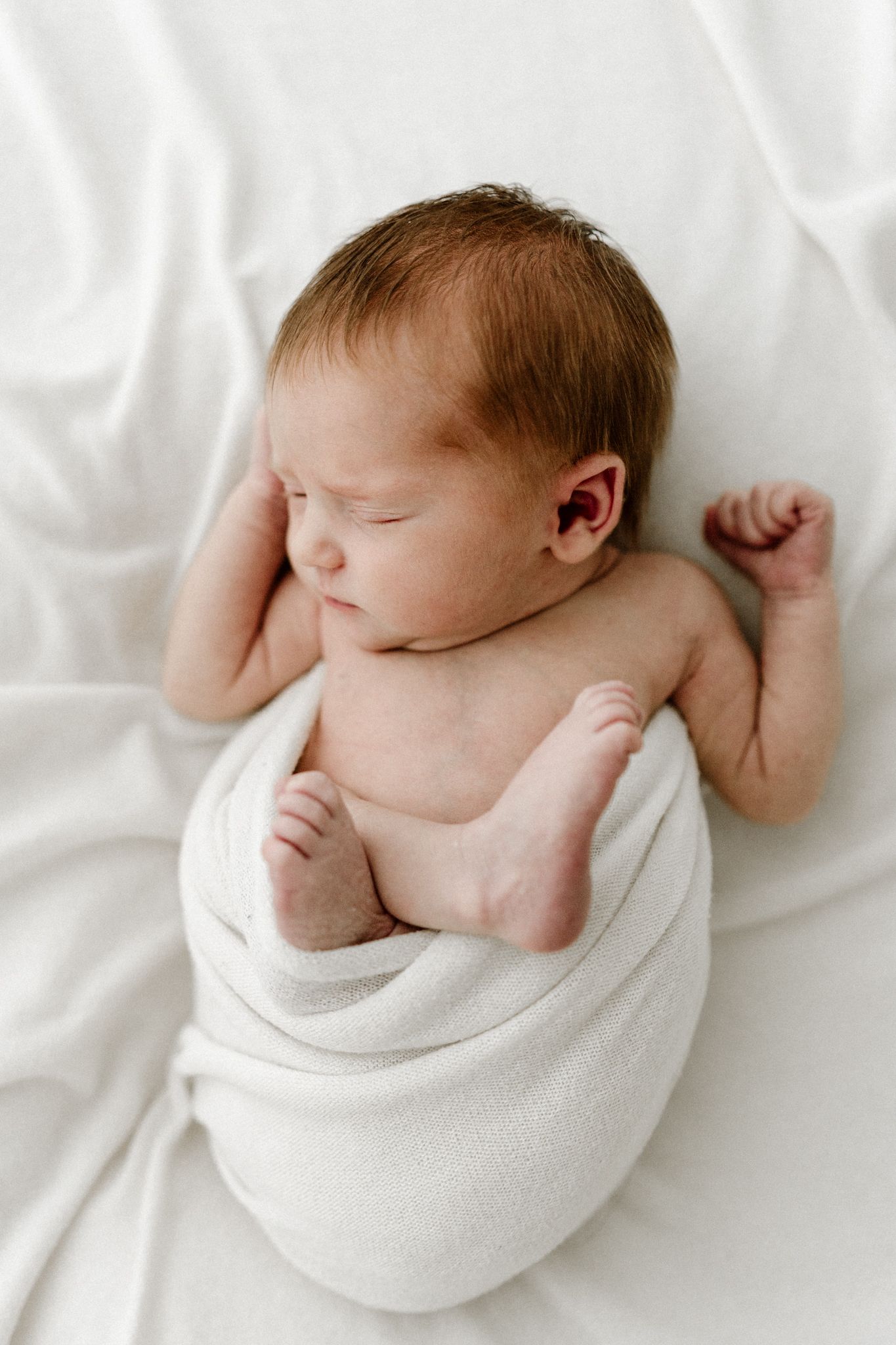 Peaceful newborn baby sleeping wrapped in white swaddle with tiny feet peeking out.
