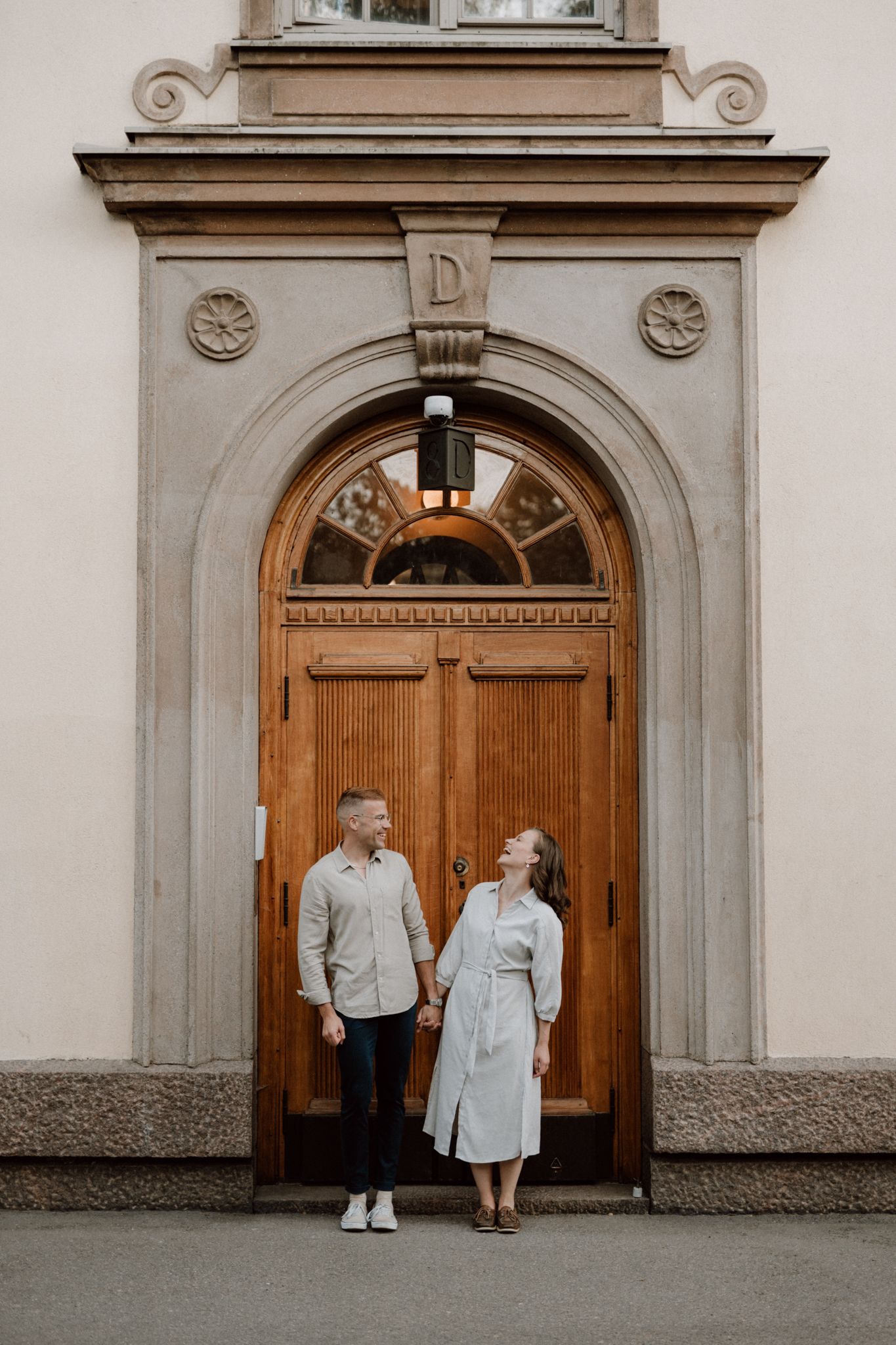 Couple holding hands and smiling at each other before an elegant arched wooden doorway.