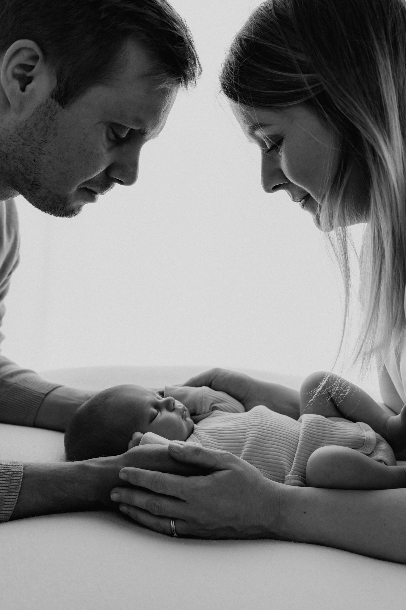 Black and white photo of parents lovingly gazing at sleeping newborn baby.