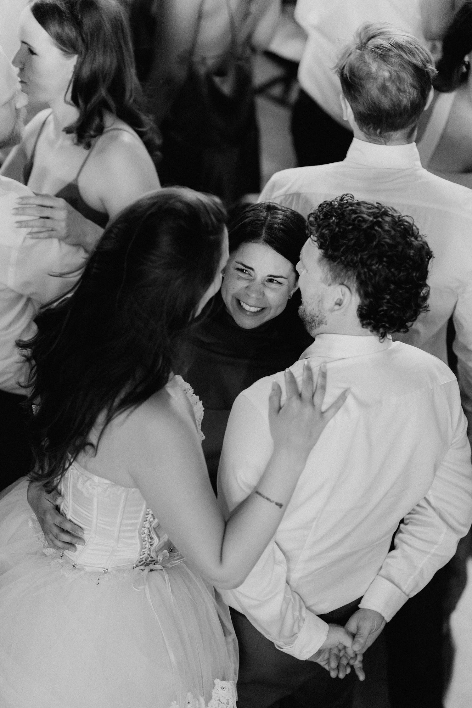 Black and white overhead shot of bride and groom dancing and laughing with a smiling guest.
