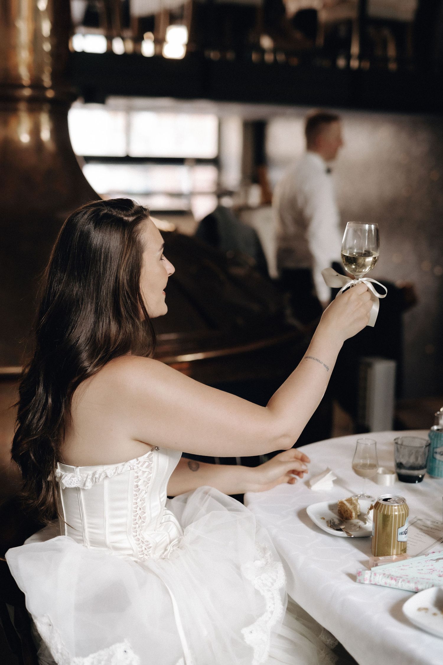 Radiant bride in white corset dress raising champagne glass in toast at reception.