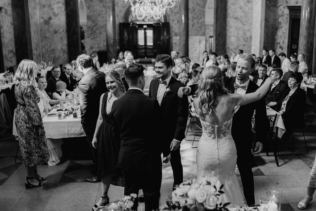 Black and white photo of bride and groom greeting guests at elegant wedding reception.