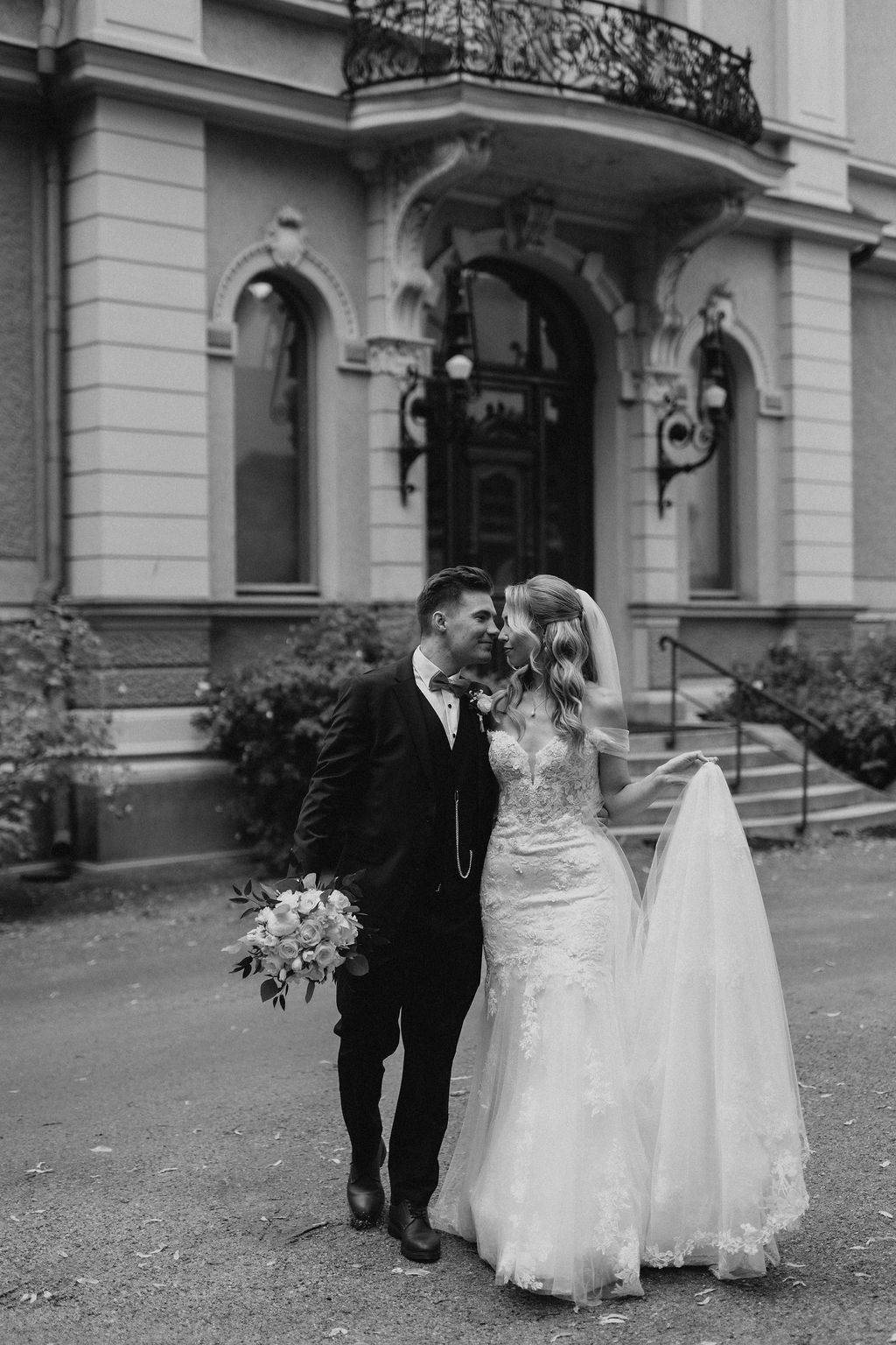 Black and white photo of bride and groom sharing a romantic moment outside a grand historic building.