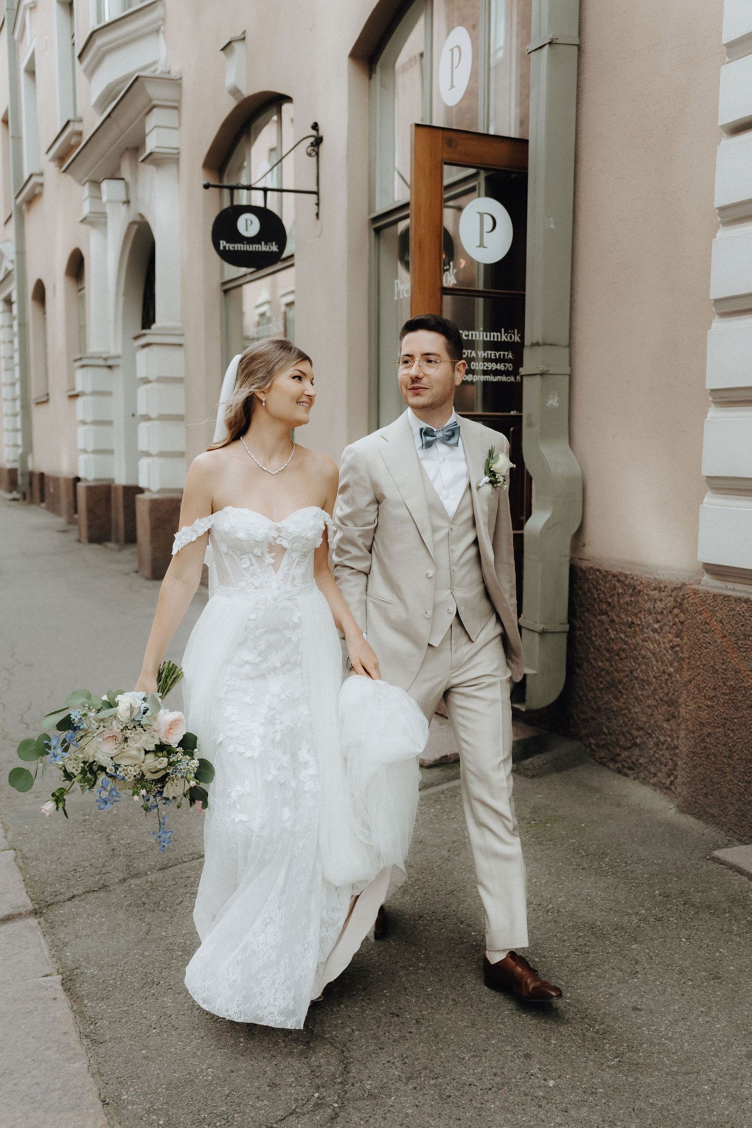 Bride and groom walking together on a city sidewalk, bride holding a blue and white bouquet.