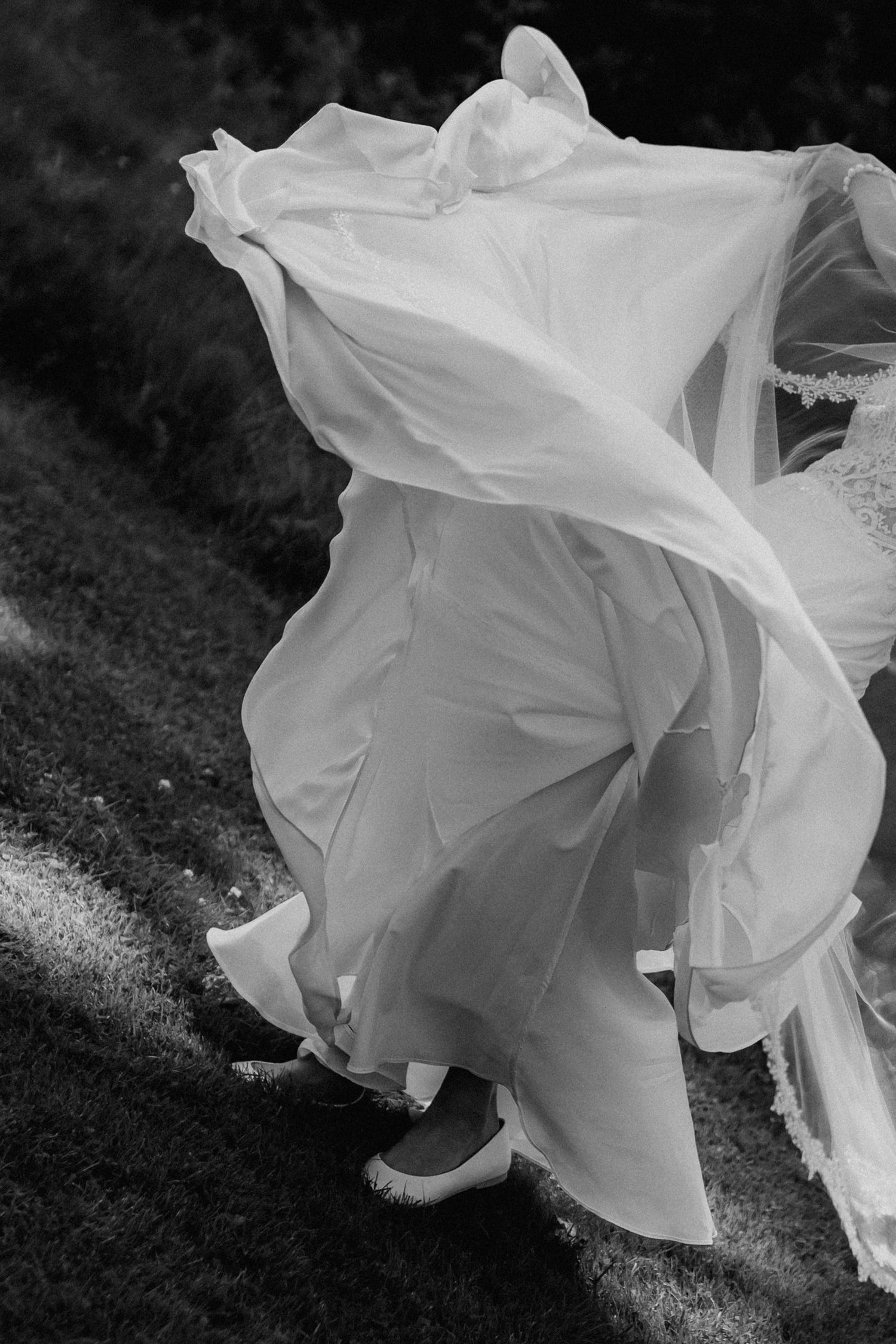 Artistic black and white close-up of a flowing white wedding dress and veil caught in the wind outdoors.