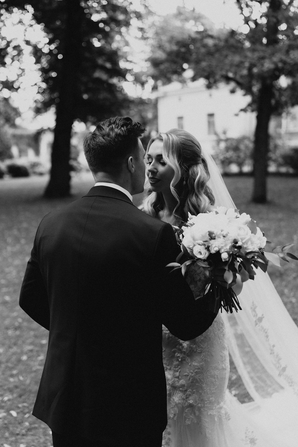 Romantic black and white photo of bride and groom about to kiss in a garden setting.