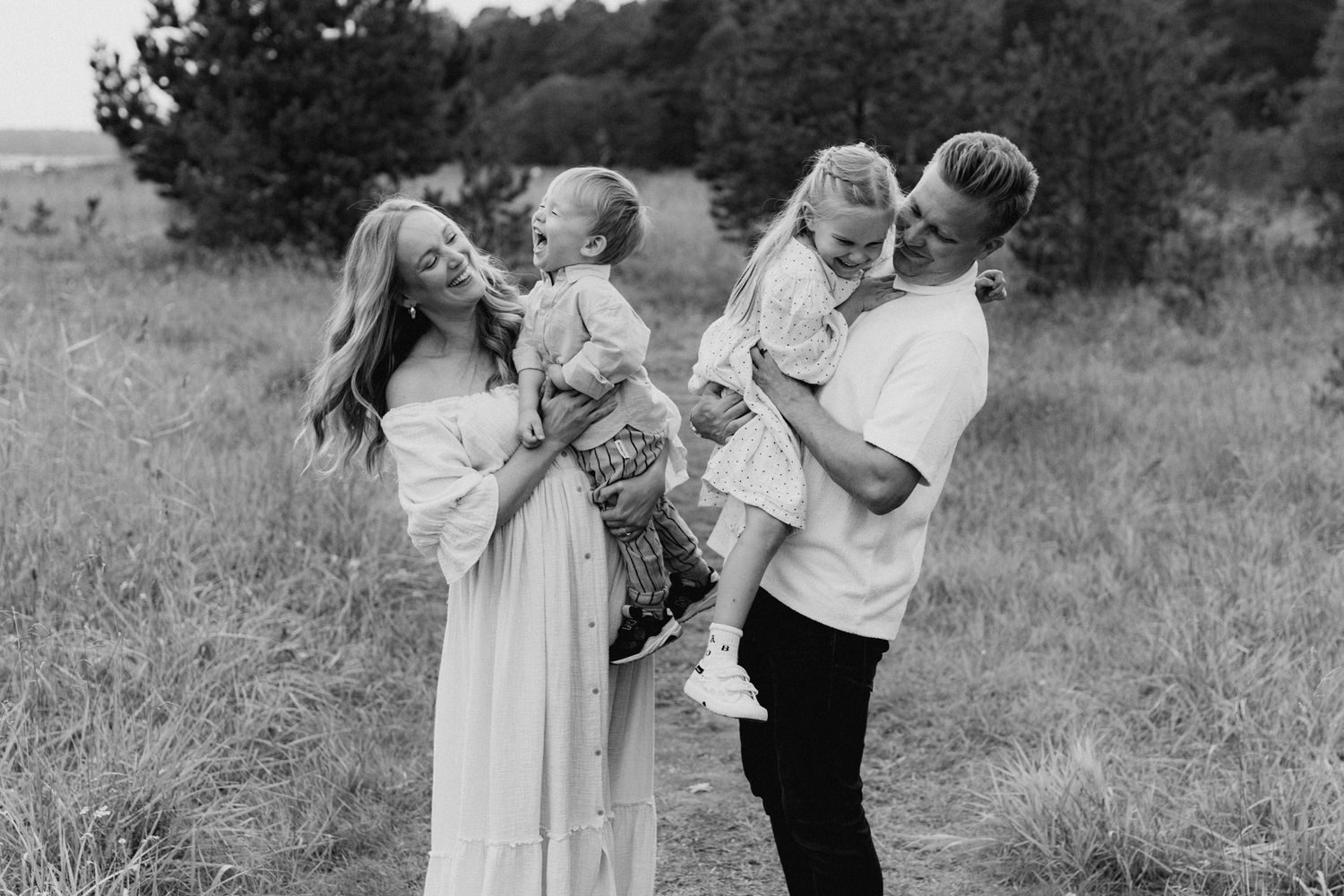 Black and white family photo of parents holding two young children in a grassy field.