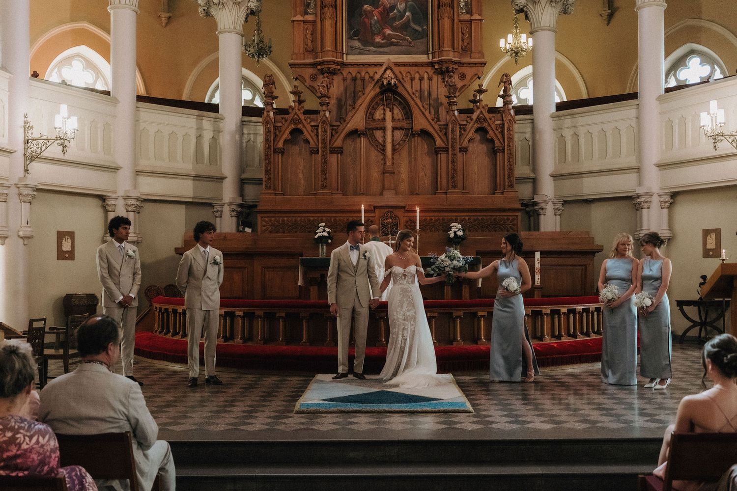 Wedding ceremony at ornate church altar with bride, groom, and bridesmaids in blue gowns.