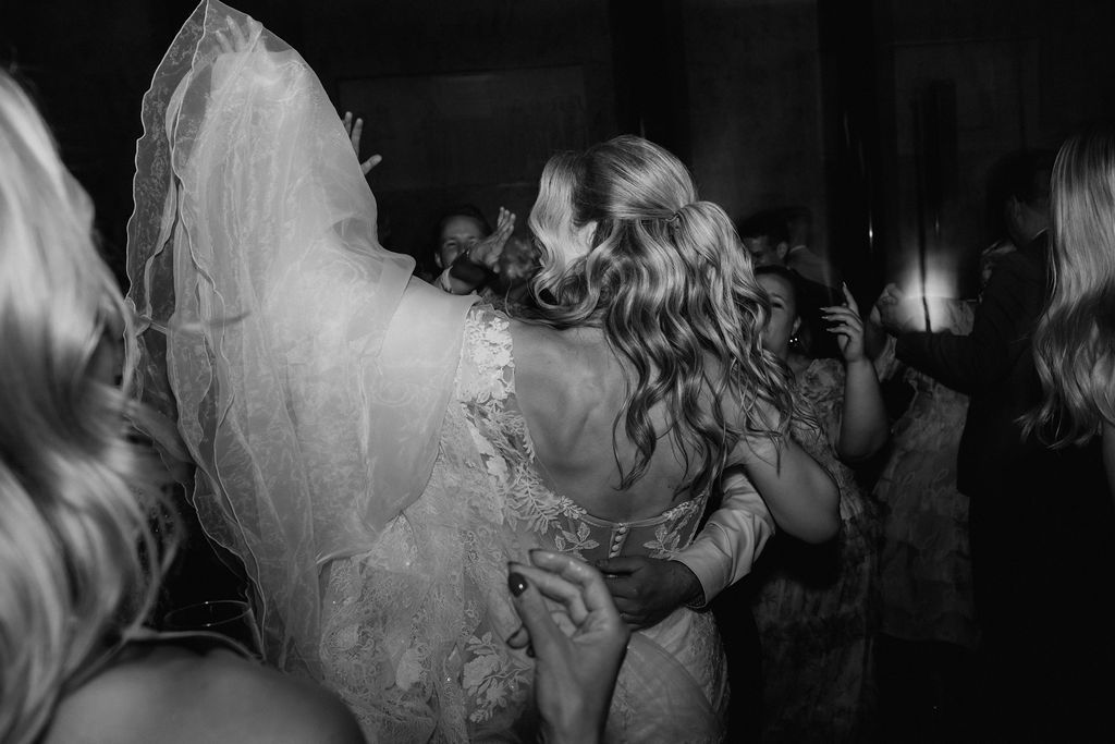 Black and white photo of bride in lace wedding gown embracing a guest on the dance floor.