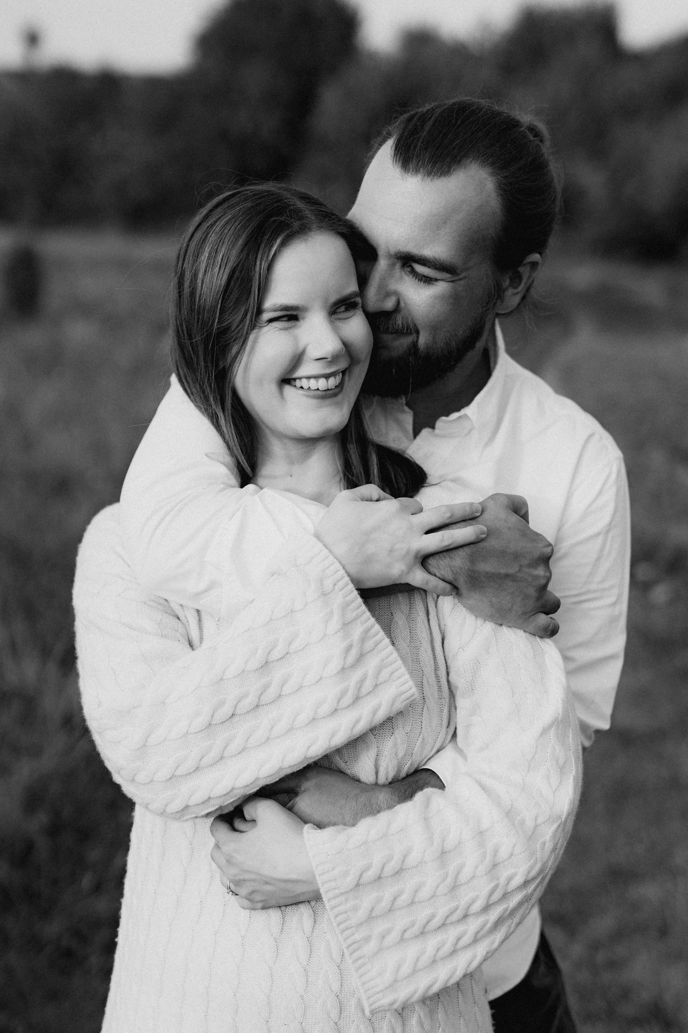 Black and white image of a couple laughing and embracing warmly in a field.
