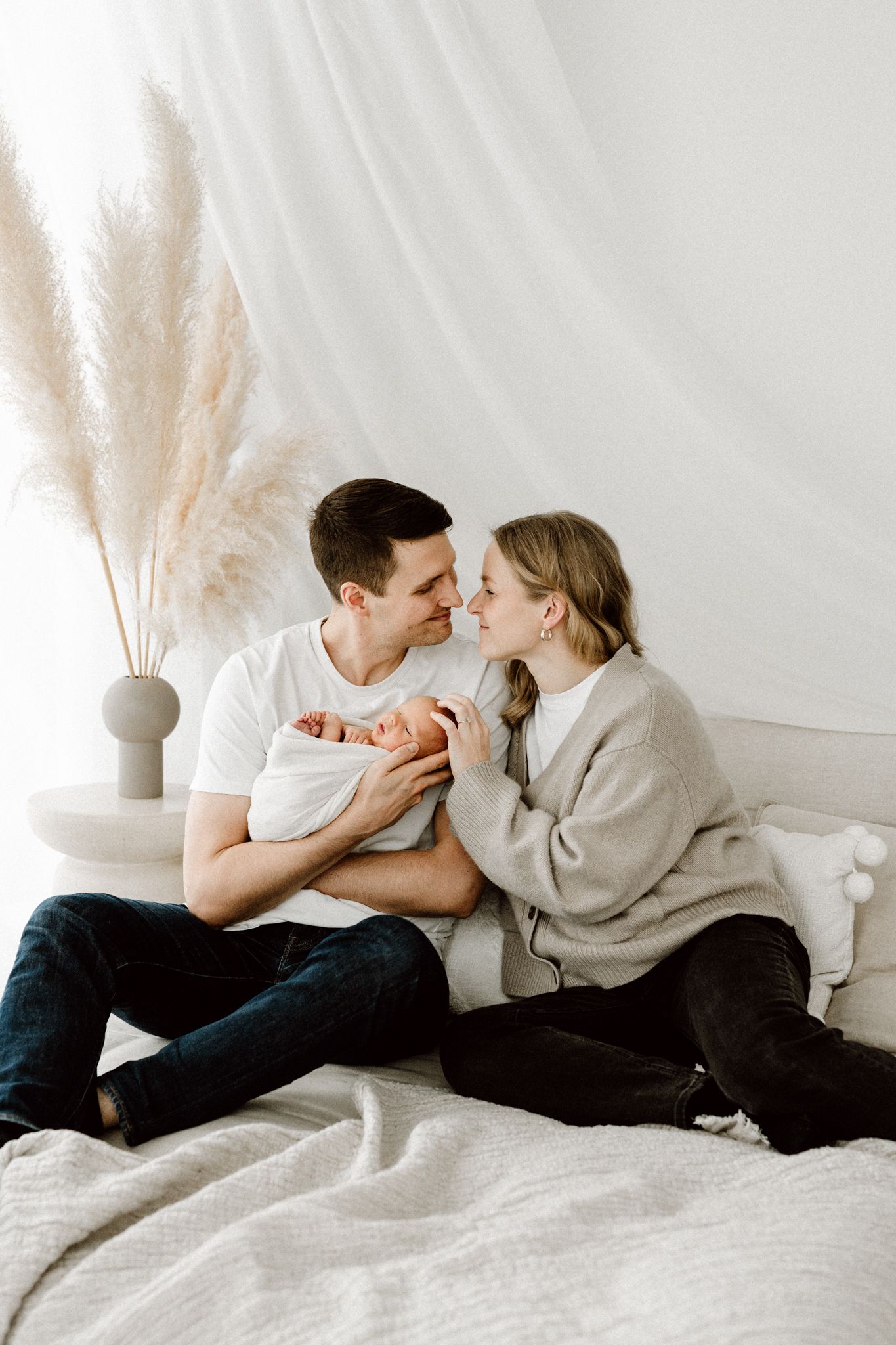 Young couple sitting on bed sharing a tender moment while holding their newborn baby together.