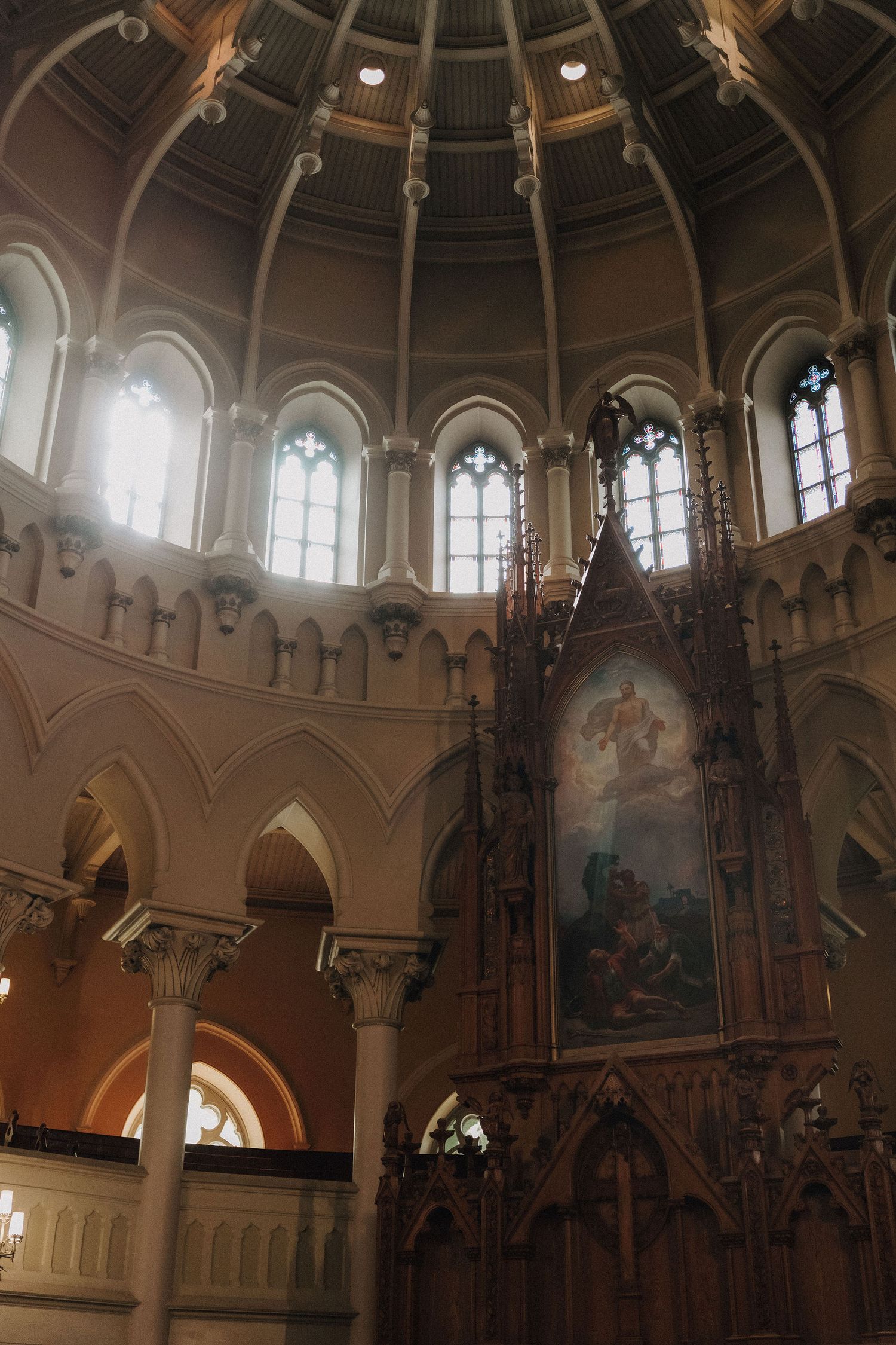 Interior view of church dome ceiling with arched windows, ornate columns, and large religious painting above the altar.