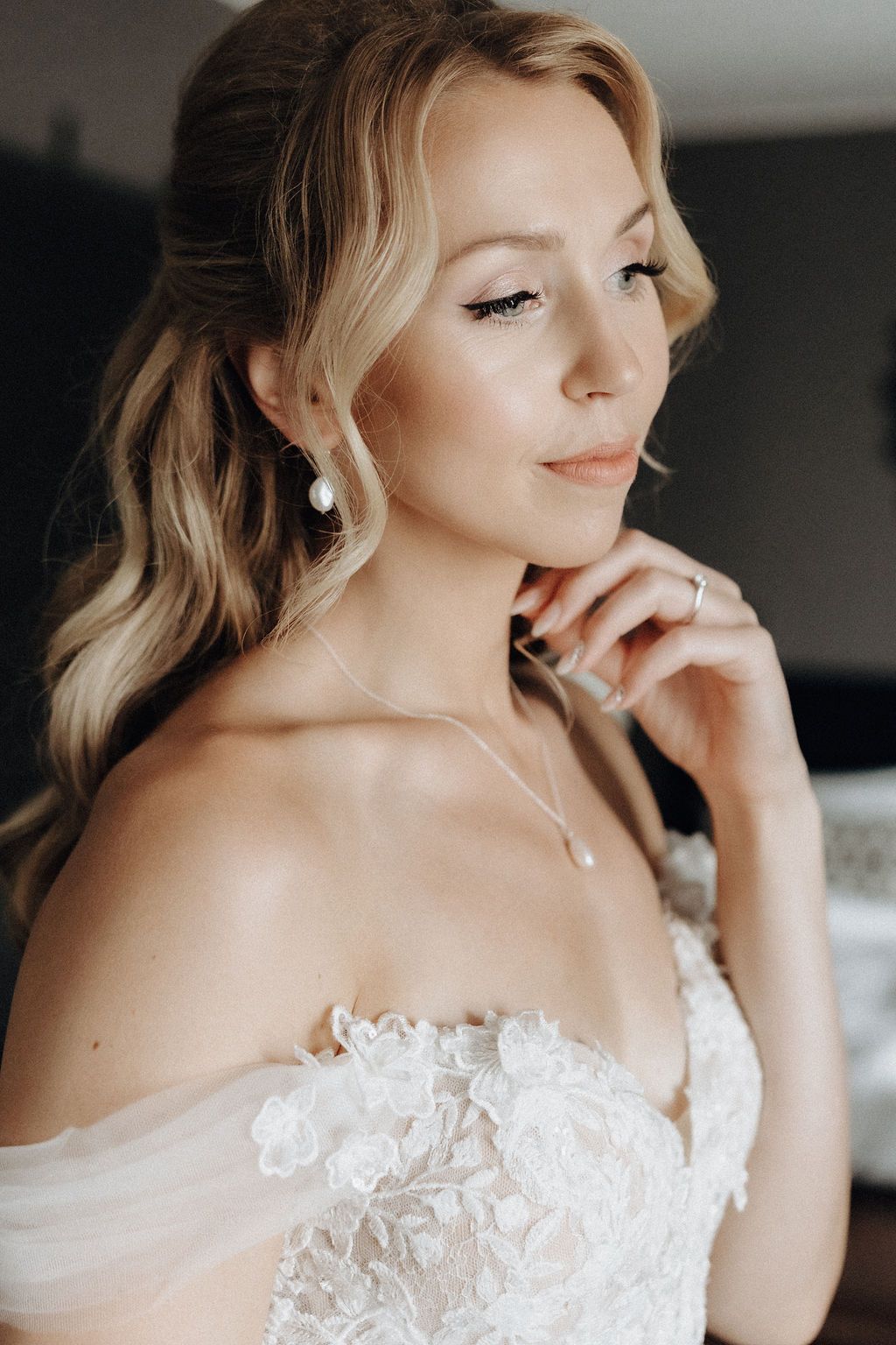 Close-up portrait of radiant bride wearing pearl drop earrings and lace wedding dress.